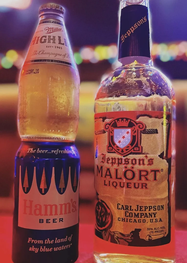 Miller High Life bottle inverted in Hamm's can, next to Malört bottle.