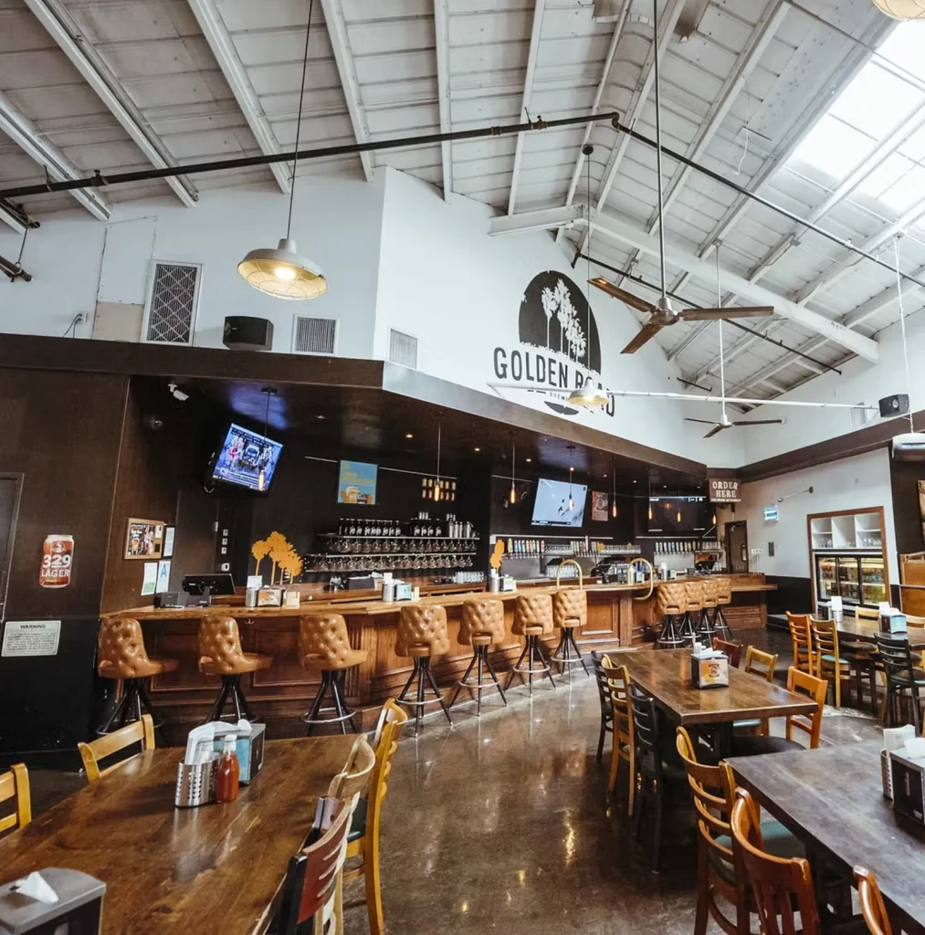Spacious industrial brewpub with Golden Road Brewery logo, bar, tables.