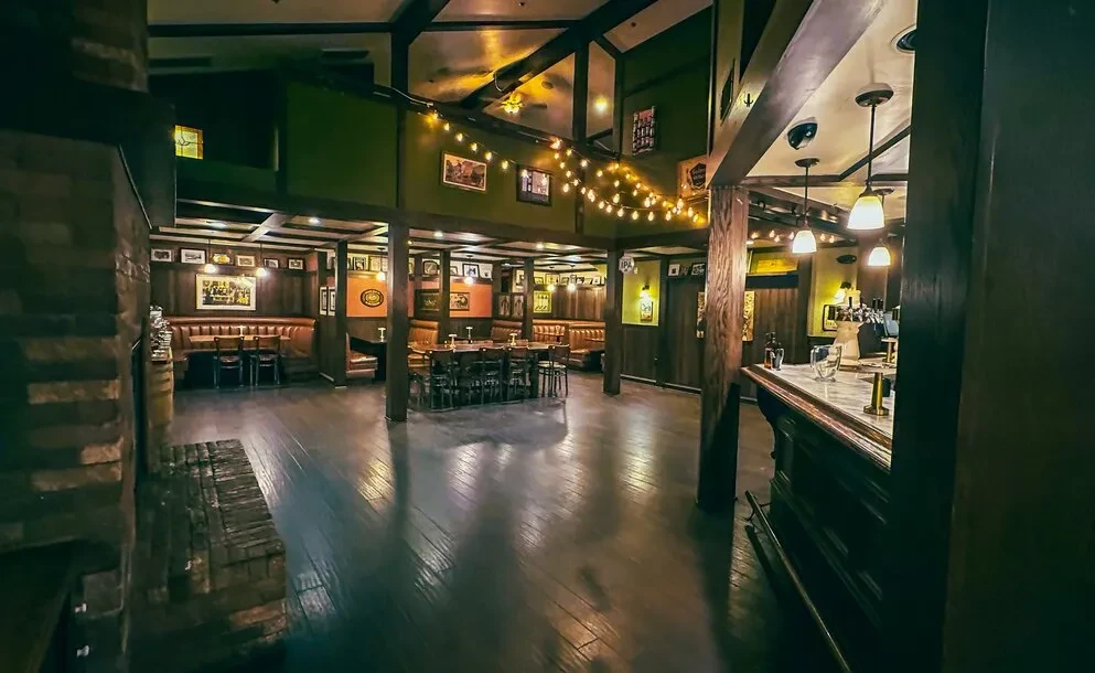 Rustic multi-level pub interior, empty, with dark wood and warm string lights.