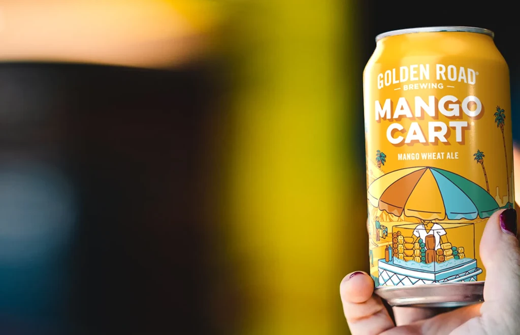 Hand holds a yellow can of Golden Road Mango Cart ale.