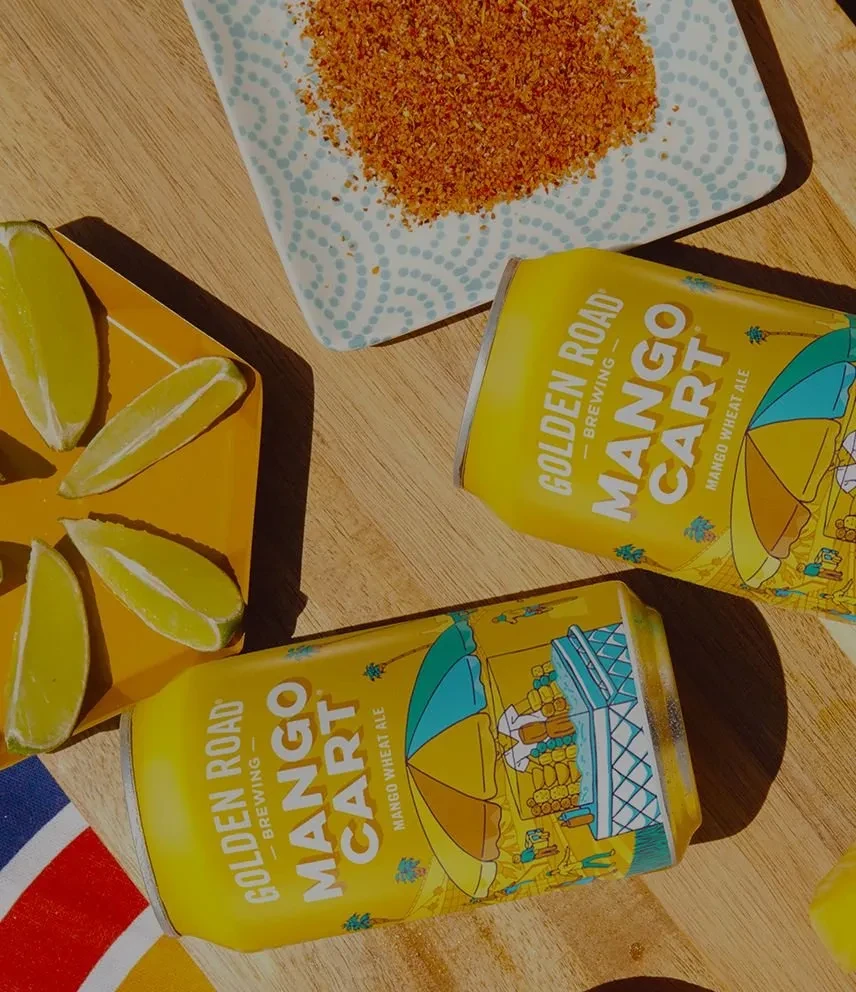 Two yellow Mango Cart beer cans with lime and chili-lime seasoning.