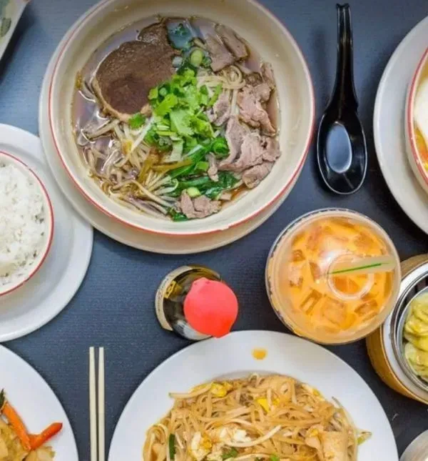 Flat lay of beef noodle soup, stir-fried noodles, white rice, and iced tea.