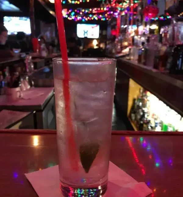 Iced drink with lime, red straw on bar, colorful bokeh lights.