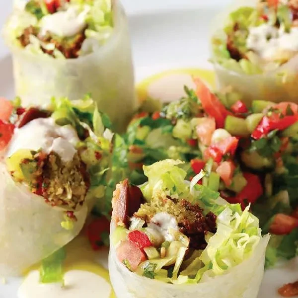 Fresh falafel spring rolls with vegetables, sauce, and side salad.