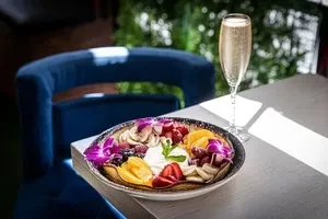 Fruit-topped pancake with orchids and sparkling drink on an outdoor table.