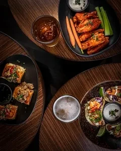 Overhead view of varied appetizers and two beers on a dark table.