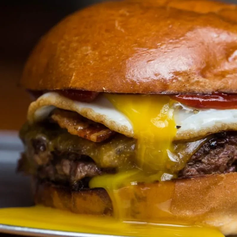 Gourmet burger with two patties, melted cheese, bacon, and oozing yolk.