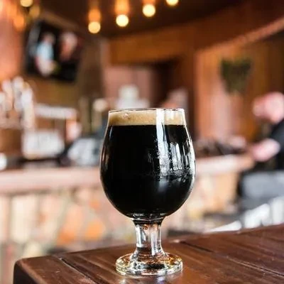 Dark beer with creamy foam on bar, blurred cozy pub background.