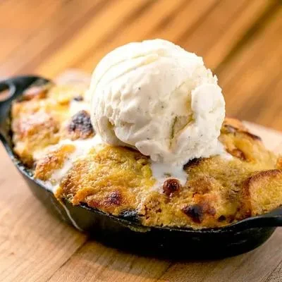Warm bread pudding with melting vanilla ice cream in a cast iron dish.