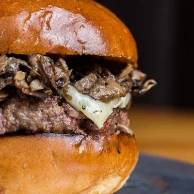 Close-up beef burger with sautéed mushrooms and melted cheese.