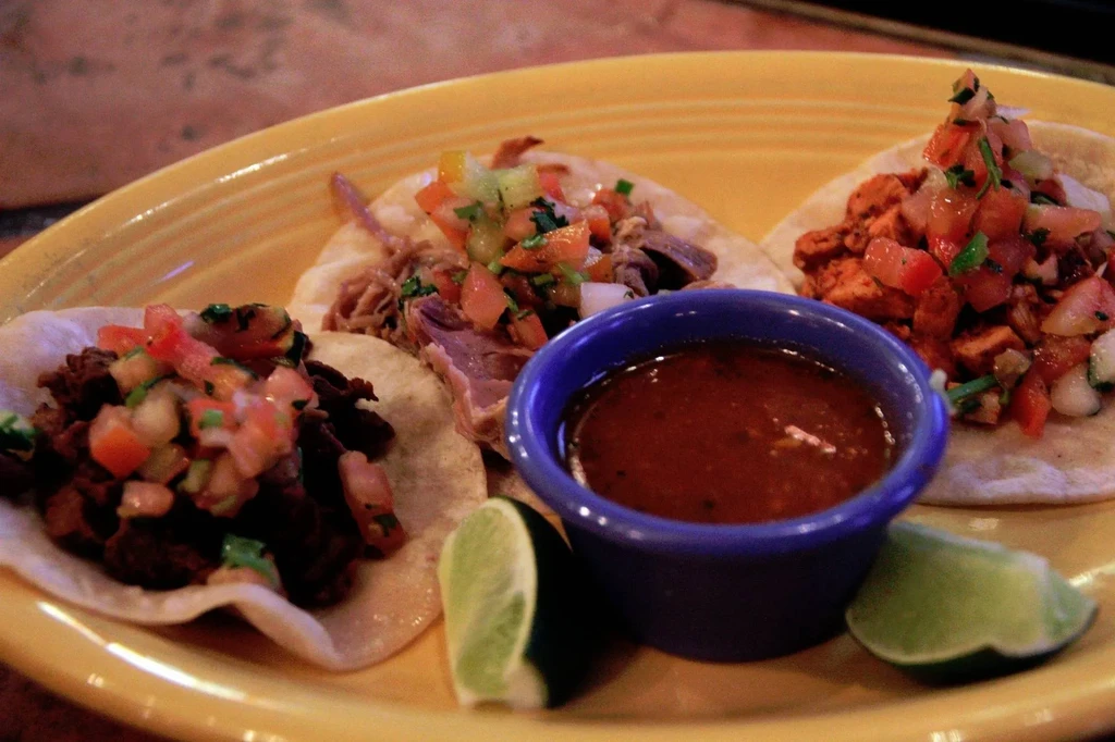 Three tacos with various fillings, pico de gallo, salsa, and lime.