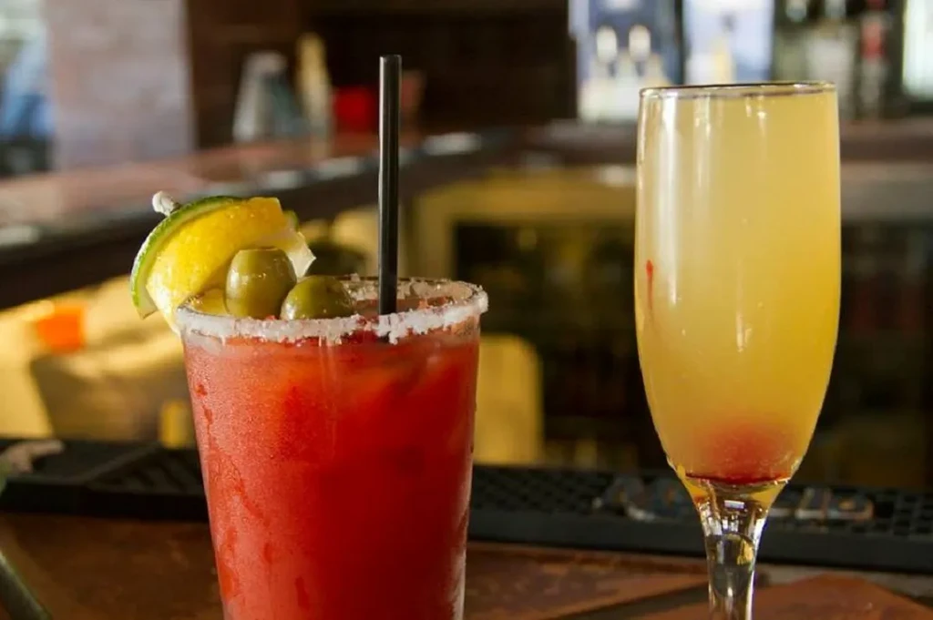 Reddish drink with lime and olives, next to a yellow flute drink.