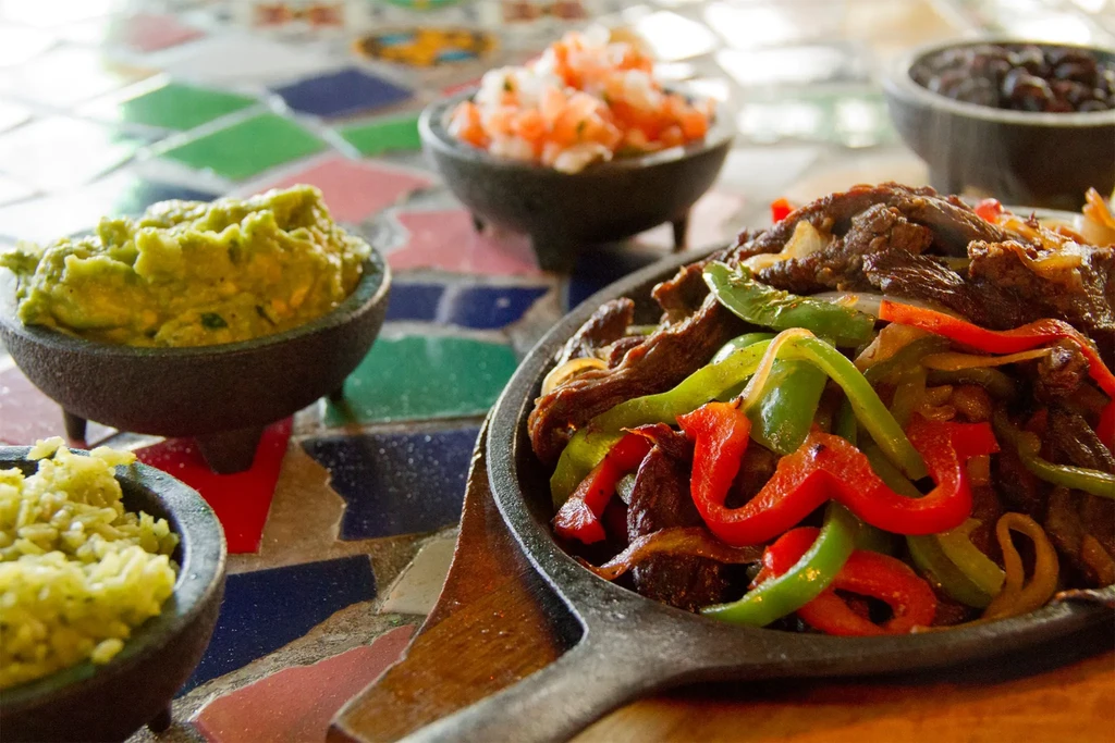 Sizzling beef fajitas and Mexican sides on a colorful tiled table.