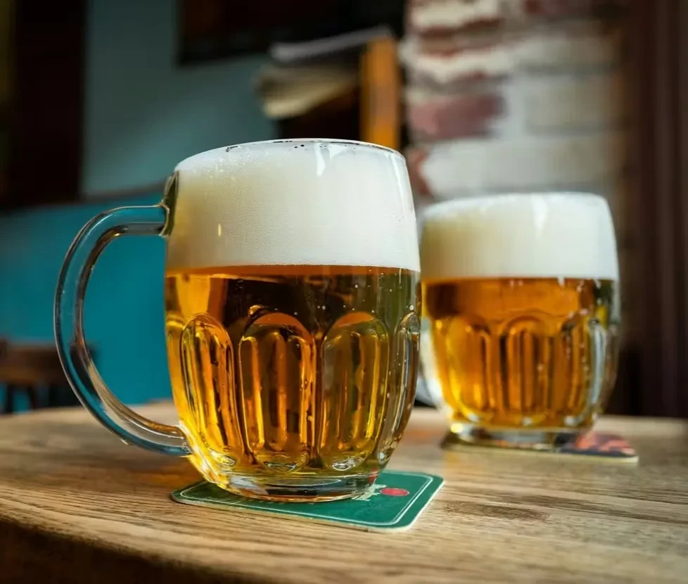 Two beer mugs with golden liquid and foam on a wooden table.