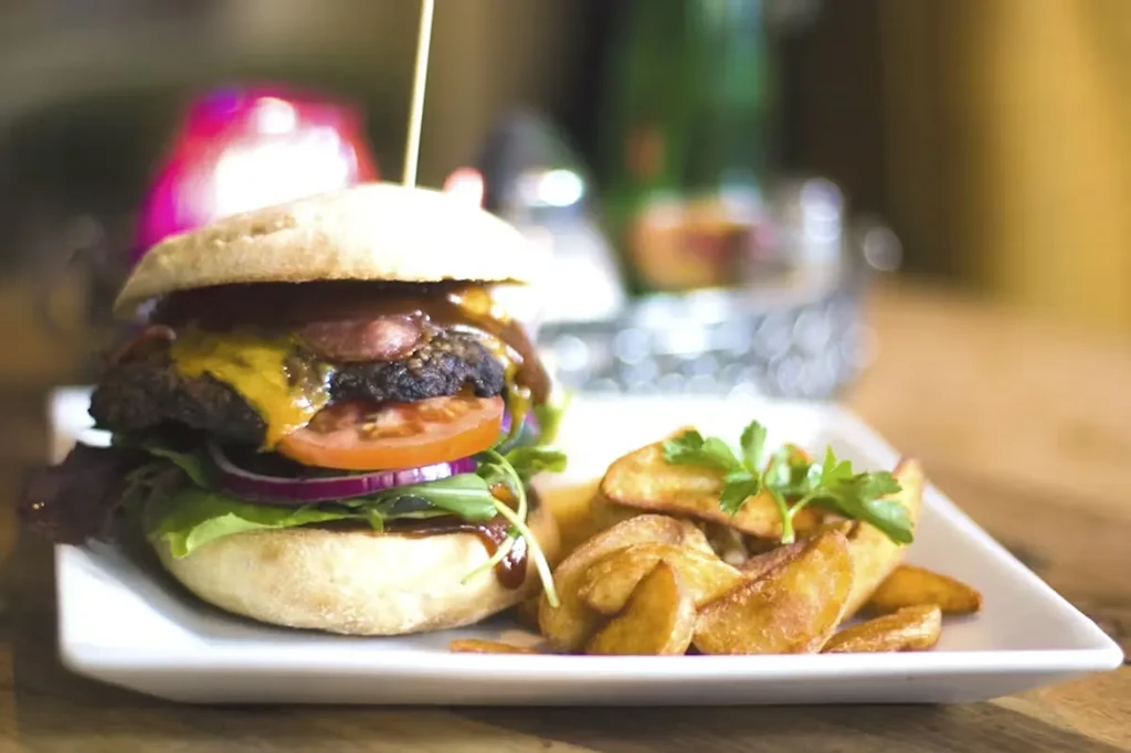 Gourmet burger, potato wedges on a plate, with blurred restaurant background.