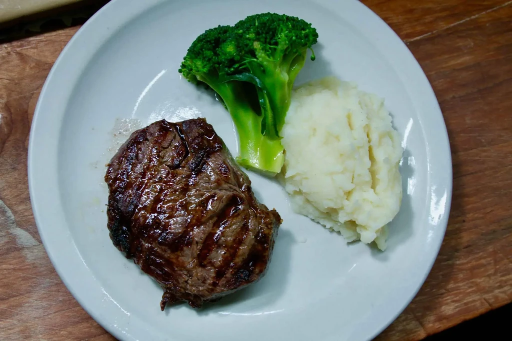 Top-down view: grilled steak, broccoli, mashed potatoes on an oval plate.