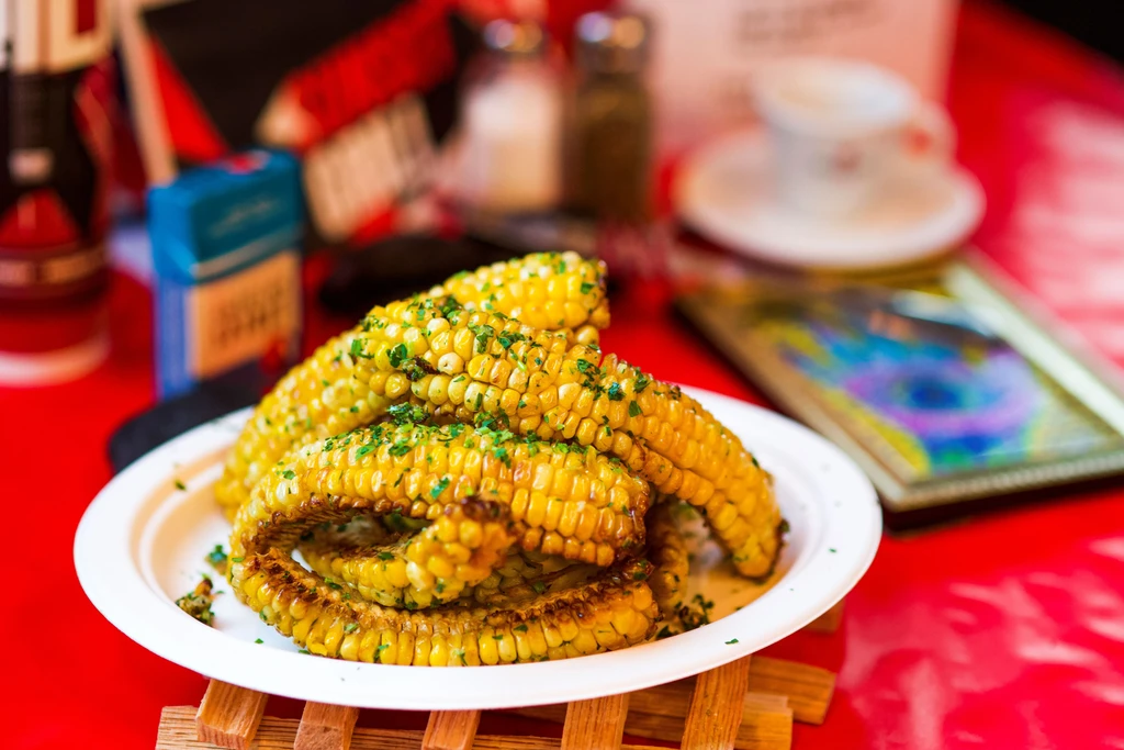 Grilled corn on the cob, herb-sprinkled, stacked on a white plate.