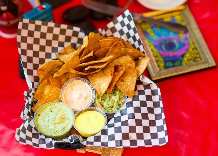 Golden-brown tortilla chips with three colorful dips on a red surface.