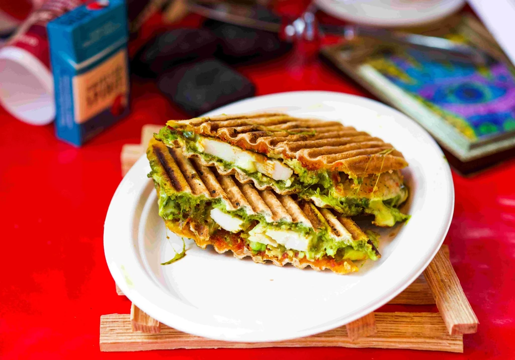 Grilled sandwich with meat, green spread, and melted cheese on a plate.