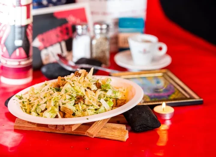 Fresh salad with crispy pieces, cheese, and herbs on a red table.