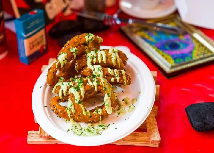 Golden fried food with green sauce, herbs, and sesame on a red table.
