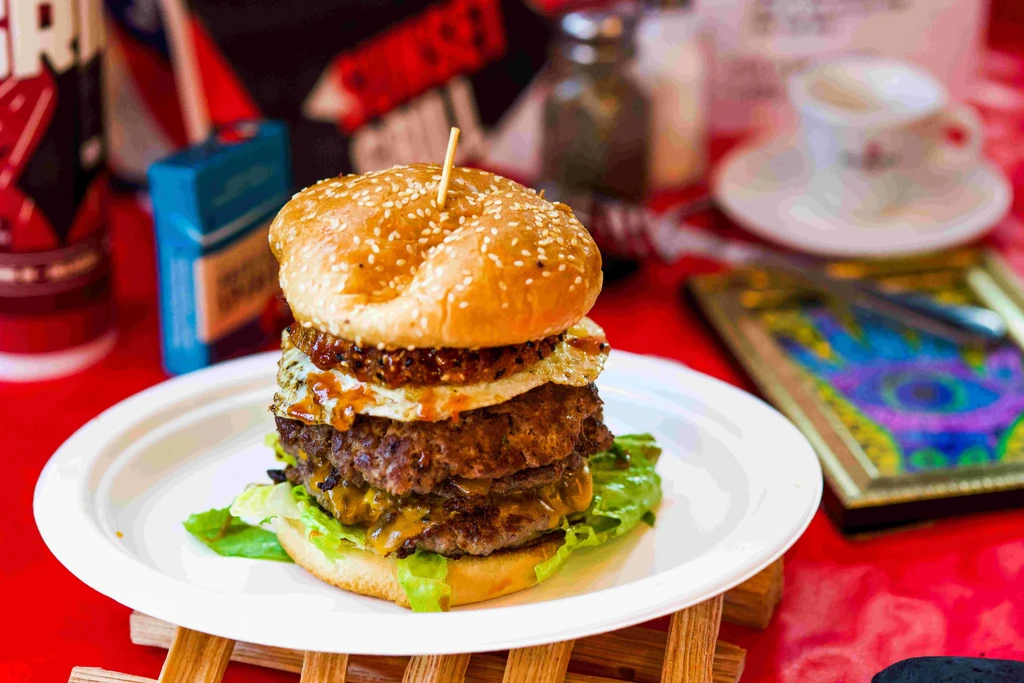 Elaborate stacked burger with three patties, cheese, fried egg, and toppings.