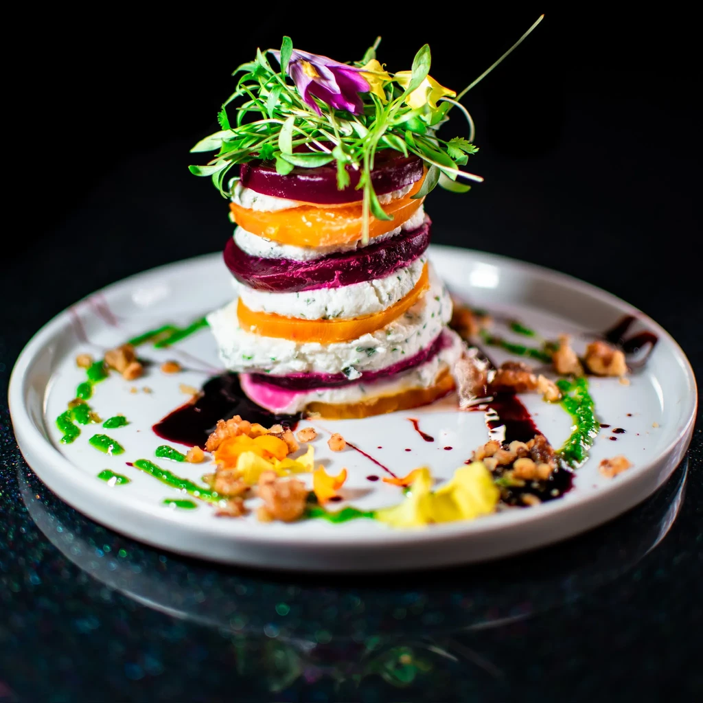 Layered beets and cheese with microgreens, flower, and artistic garnishes.