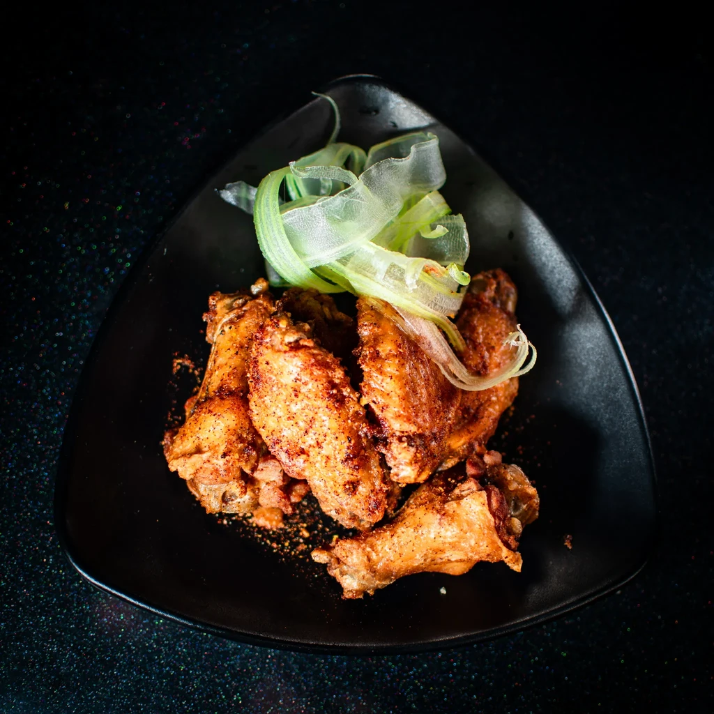 Close-up of spicy chicken wings with green garnish on a black plate.