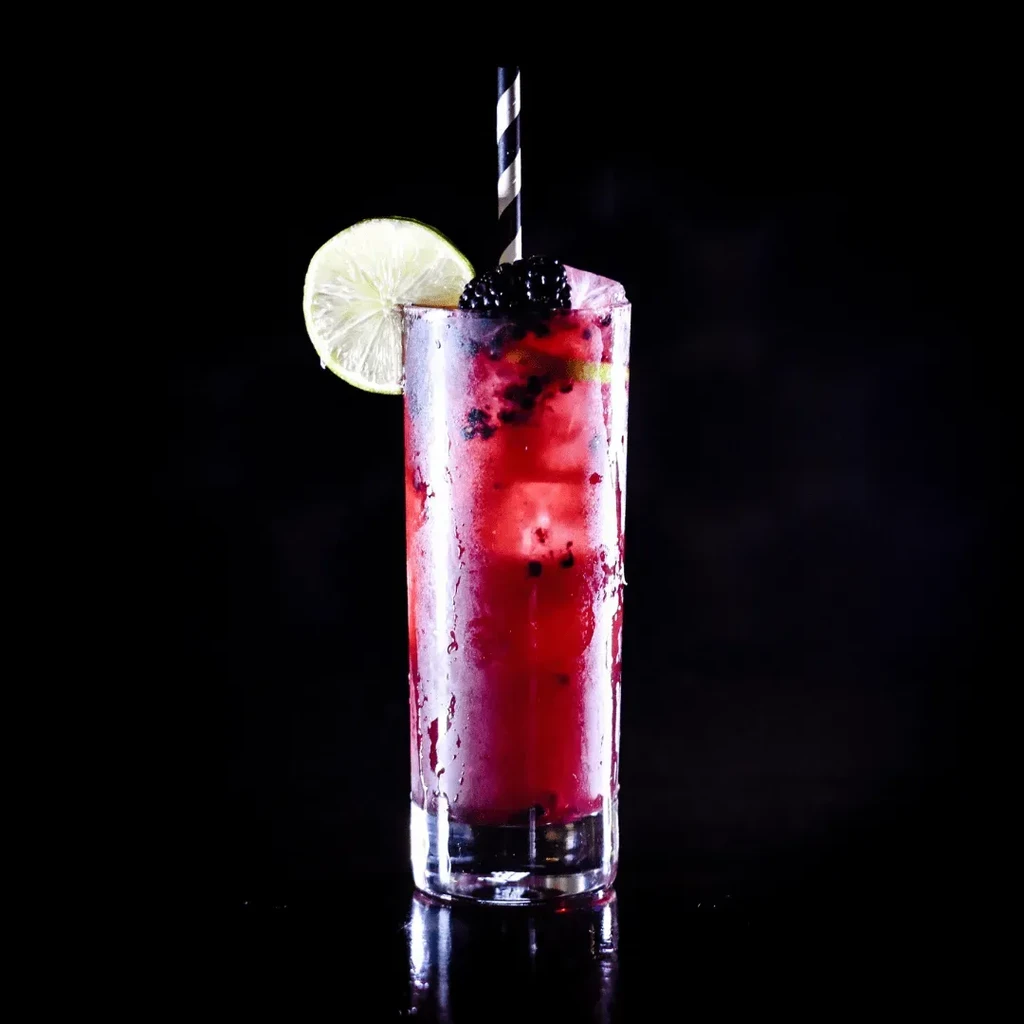Reddish-purple berry drink in glass with ice, lime, and straw.