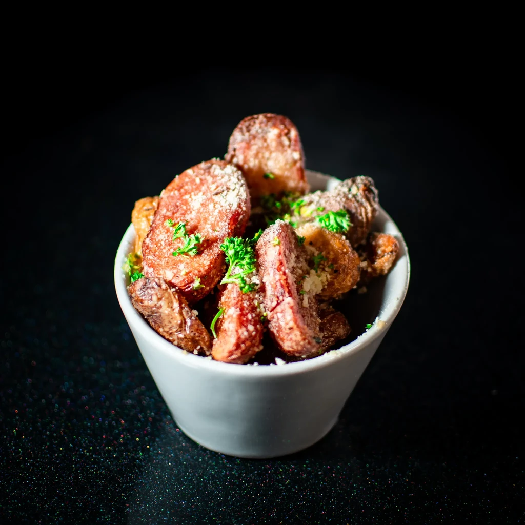 White bowl with roasted vegetables, sausage, Parmesan, and fresh herbs.