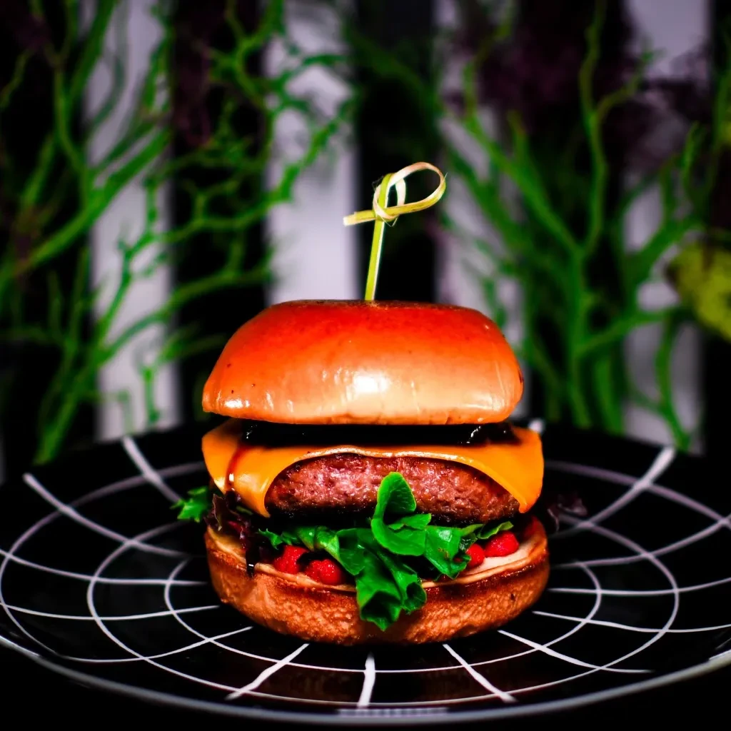 Gourmet burger with melted cheese on spiderweb plate, dark background.