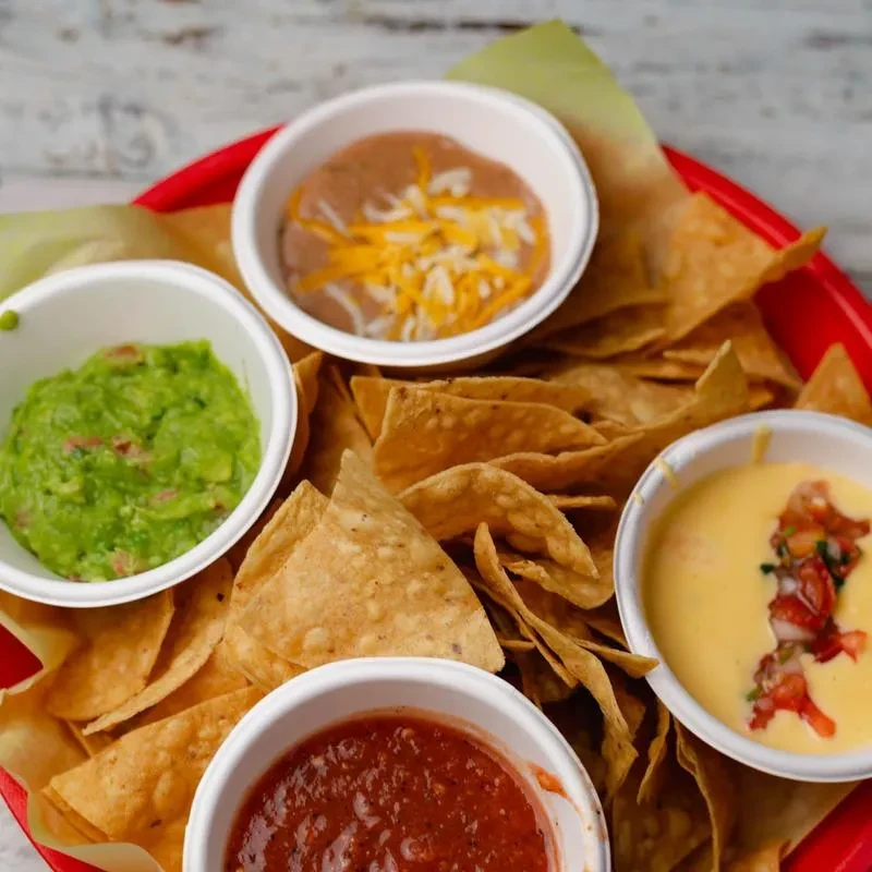 Tortilla chips with four dips: guacamole, beans, queso, and salsa.