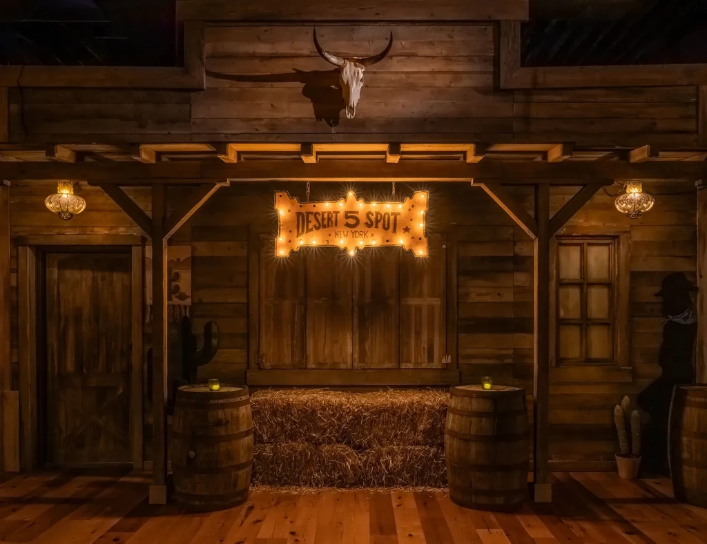 Rustic Western saloon interior with "DESERT 5 SPOT" sign, bull skull, and hay.