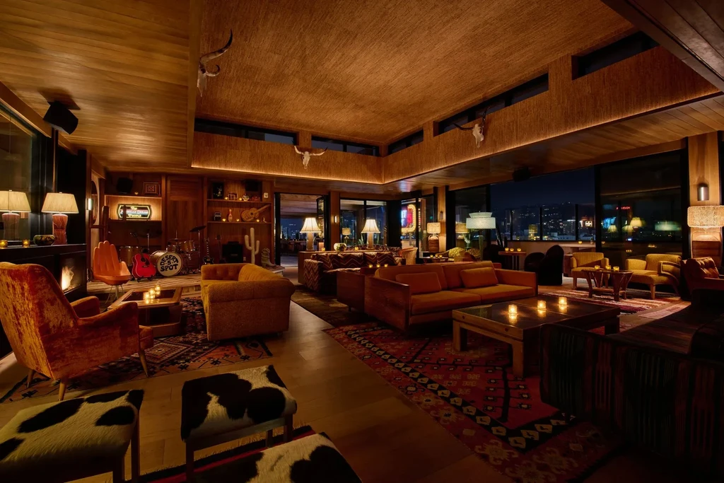 Eclectic, dimly lit lounge with Desert Spot stage, fireplace, city skyline.