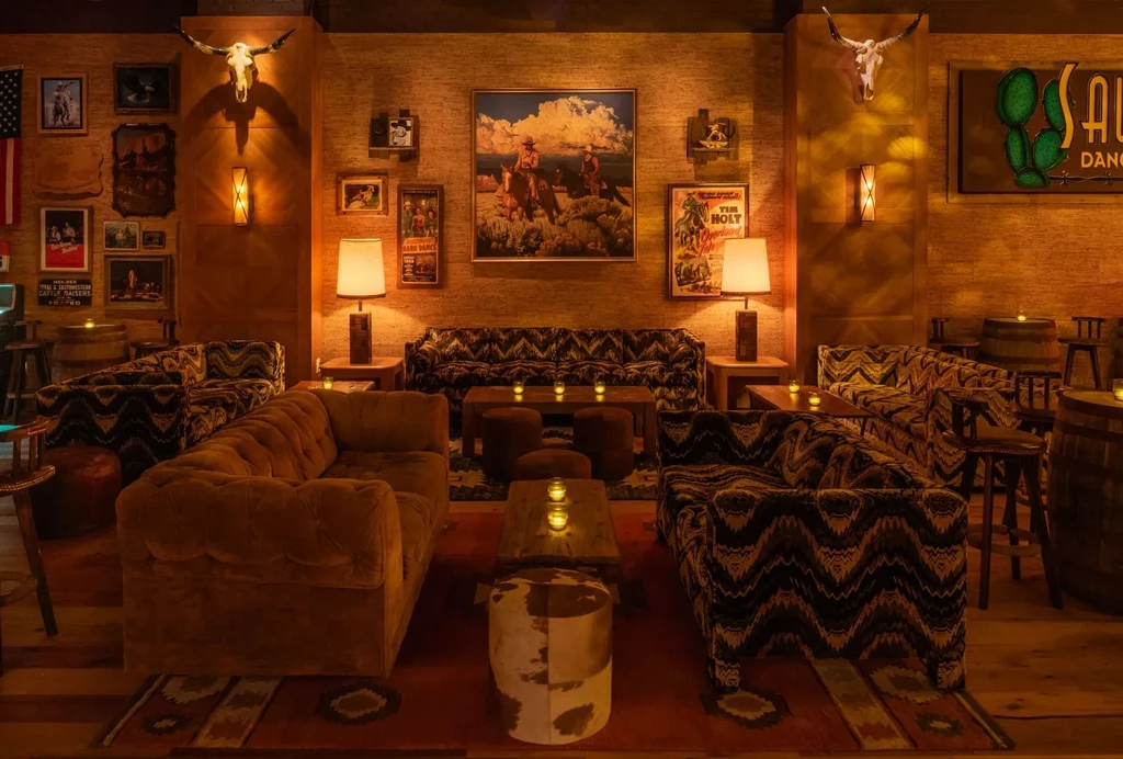 Western-themed lounge with warm lighting, velvet sofas, cowboy art, and longhorn skulls.