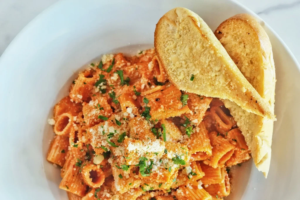 Rigatoni pasta with red sauce, cheese, herbs, and garlic bread.
