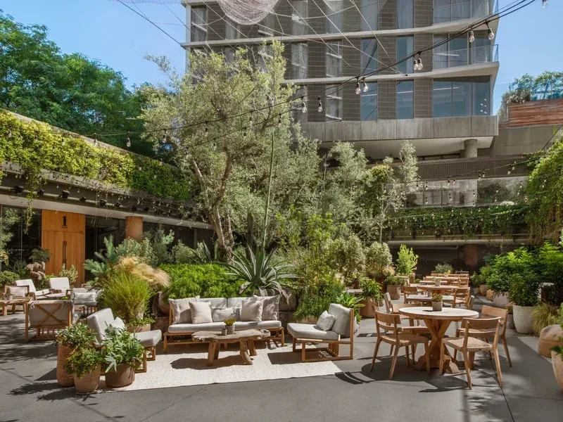 Outdoor lounge and dining area, lush plants, modern building.