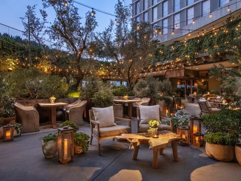 Outdoor patio at dusk with warm string lights, lush plants, and seating.
