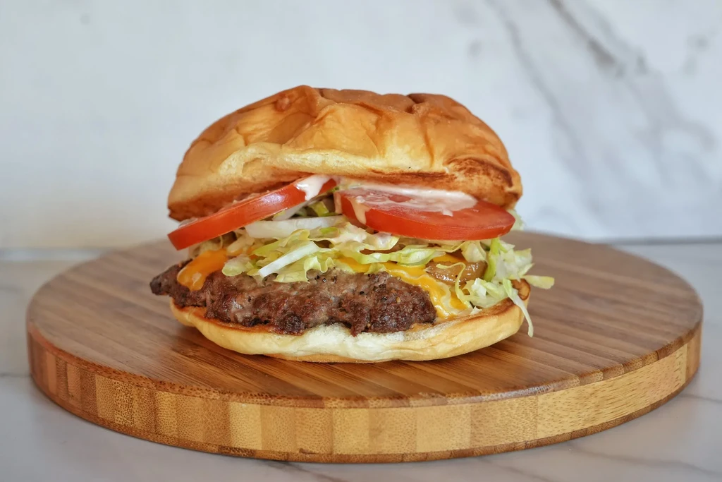 Hamburger with melted cheese, lettuce, tomato, onion, on bamboo board.