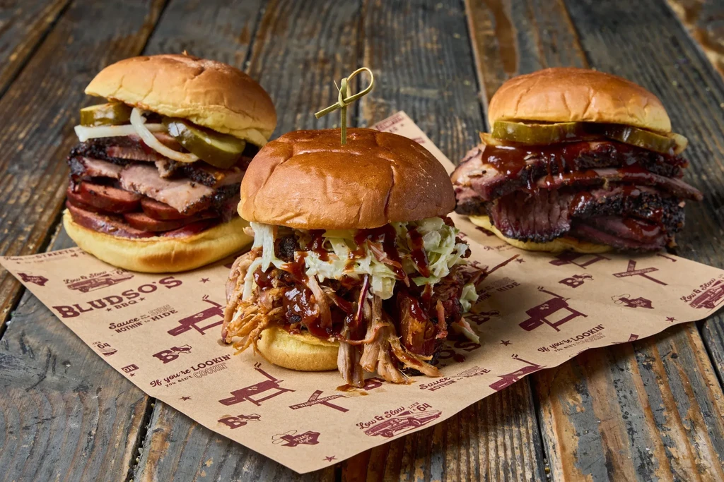 Pulled pork, brisket, and sausage BBQ sandwiches on Bludso's branded paper.