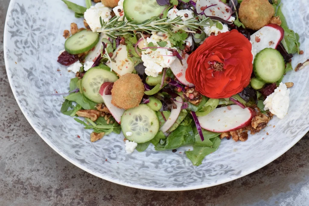 Vibrant salad with fried cheese, nuts, cranberries, and a red flower.