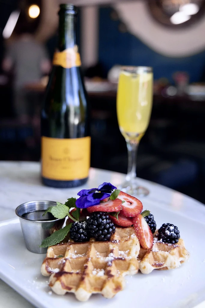 Waffles with berries and flower, champagne bottle and mimosa.