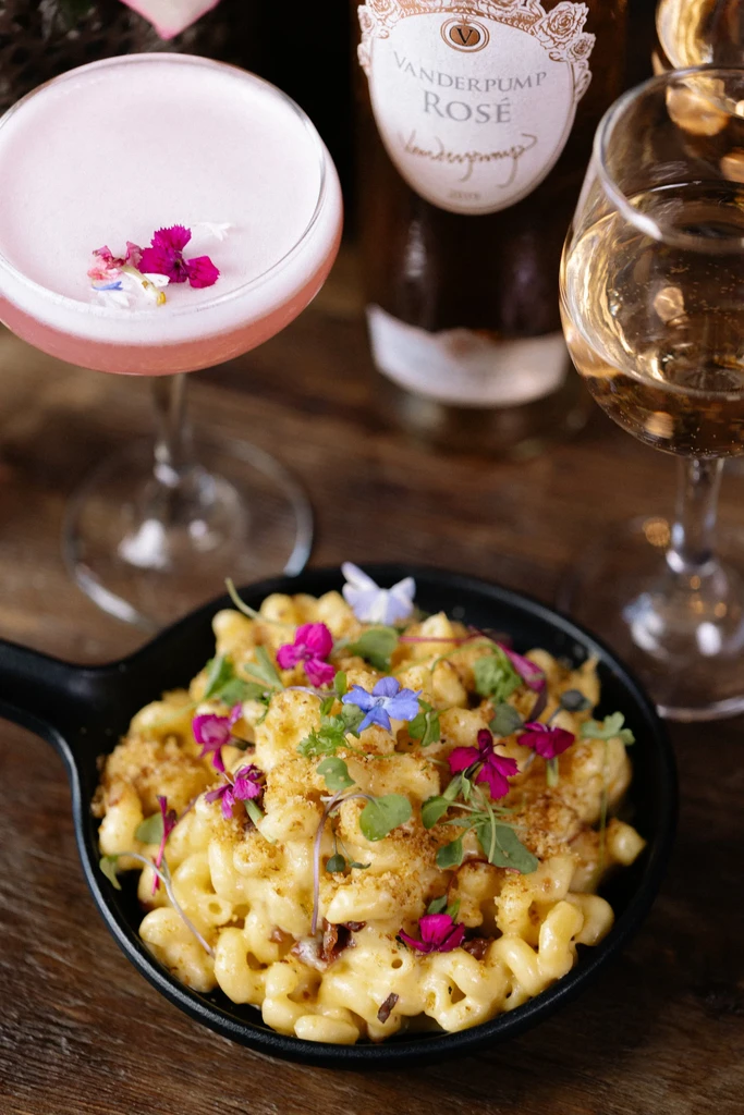 Garnished mac and cheese, pink floral cocktail, and Vanderpump Rosé bottle.