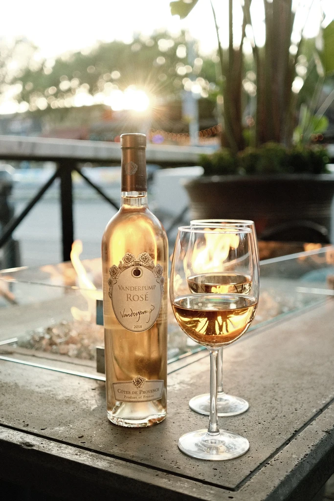 Vanderpump Rosé bottle, two glasses, outdoor fire pit, warm evening light.