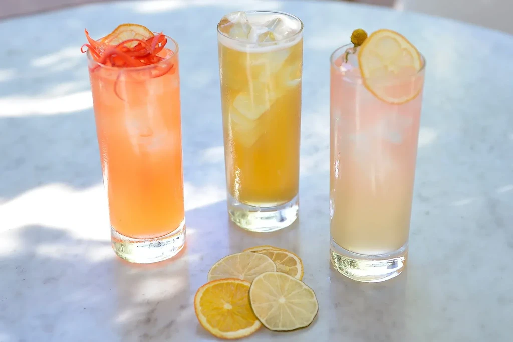 Three colorful garnished drinks with scattered dried citrus slices.