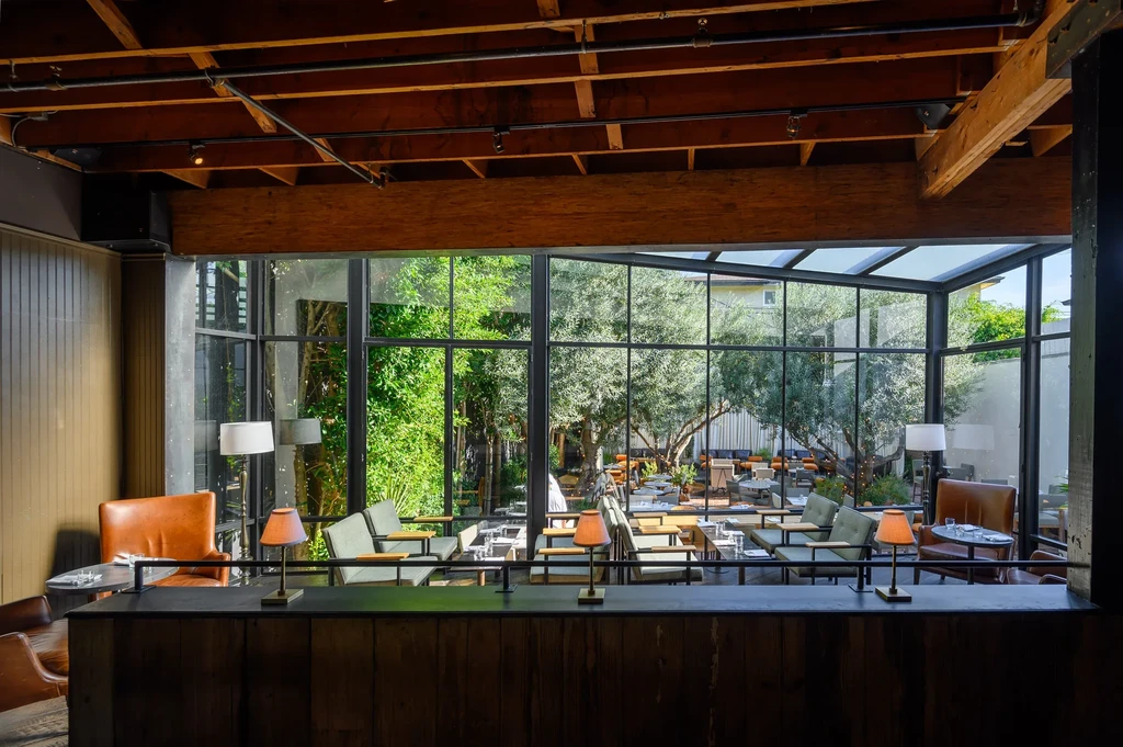 Restaurant interior with glass wall connecting to an olive tree patio.