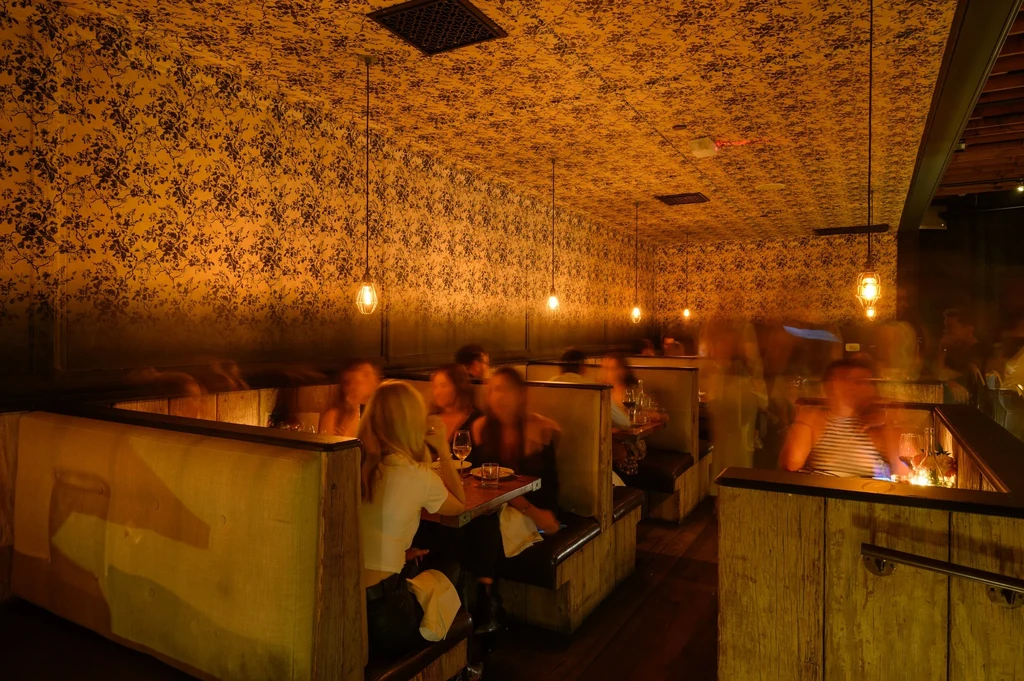 Dimly lit restaurant with floral wallpaper, wooden booths, and blurry diners.