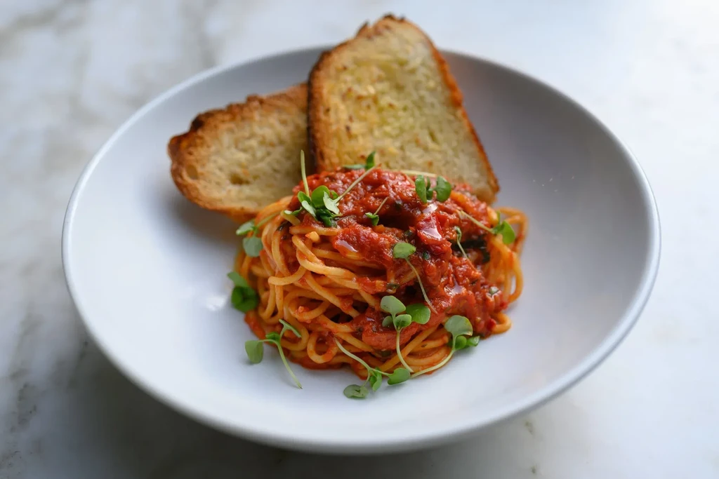 Spaghetti with tomato sauce, microgreens, and bread in a white bowl.