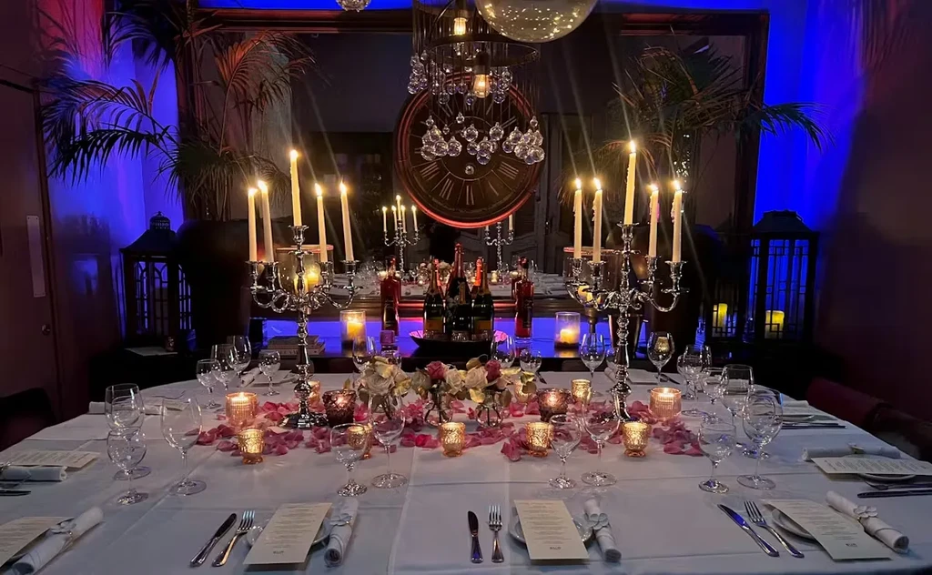 Elaborate dining table with candles, rose petals, and dramatic lighting.