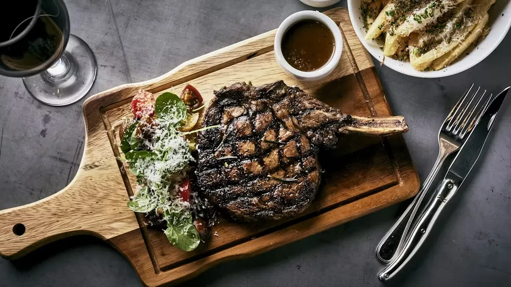 Grilled bone-in steak, side salad, fries, sauce, and red wine.